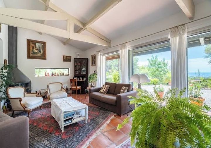Salon lumineux de la Villa L’Amalié avec poutres apparentes, poêle à bois et baies vitrées ouvrant sur le jardin